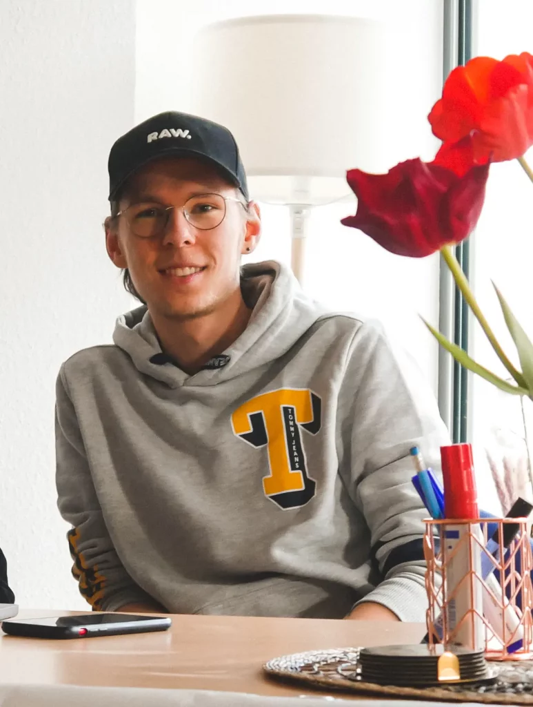 Mediengestalter des KreativHauses Friedberg lächelnd am Arbeitsplatz mit Cappy und Brille